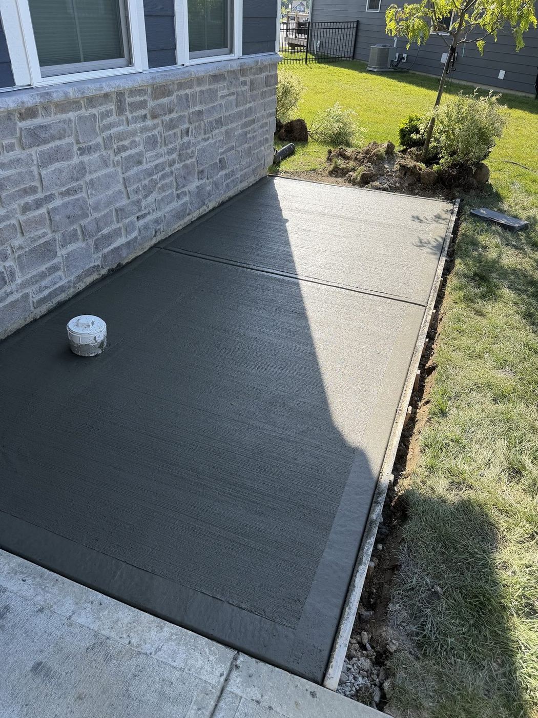 Finished poured concrete pad with a cleanout riser set flush, alongside a home