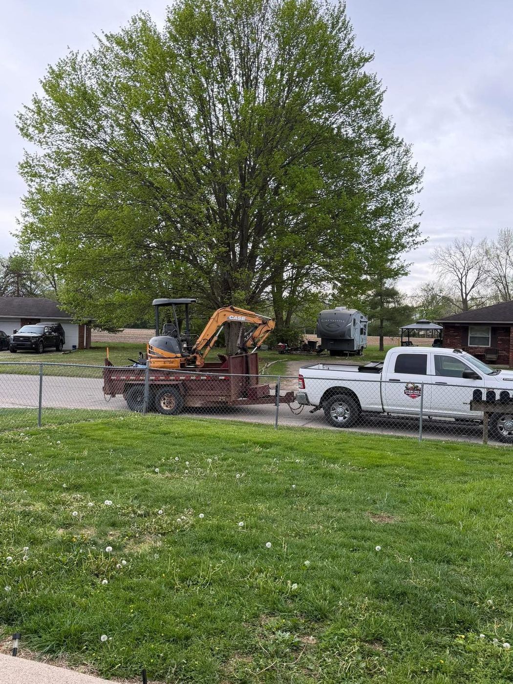 Compact excavator on a trailer behind a Sterling's pickup at a residential job site
