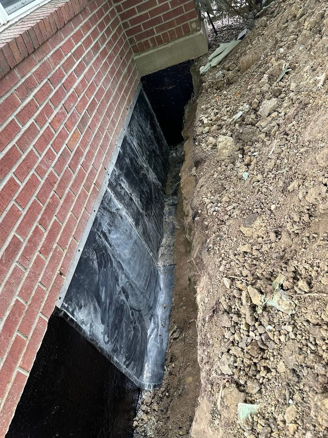 Dimple board waterproofing membrane applied to an exposed brick foundation wall in an open trench