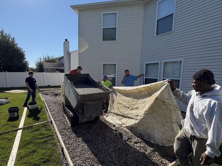 Crew placing and screeding stone base inside forms for a concrete walk