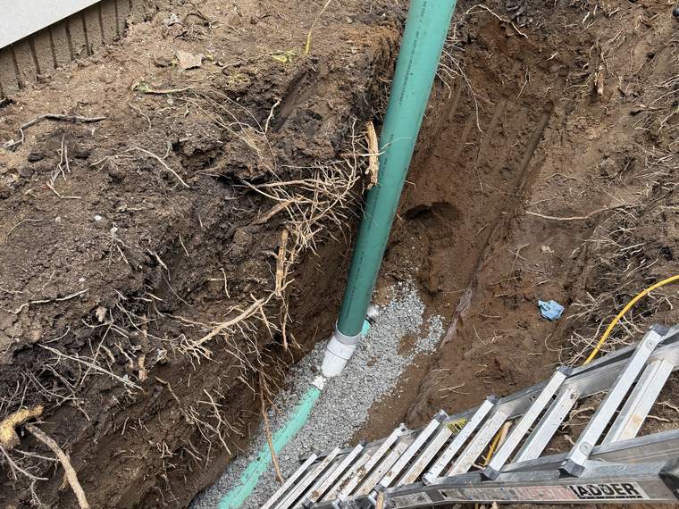 Deep excavation exposing a service line at the corner of a house