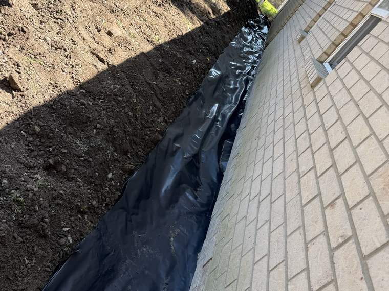 Drainage line and fabric installed alongside a paver patio