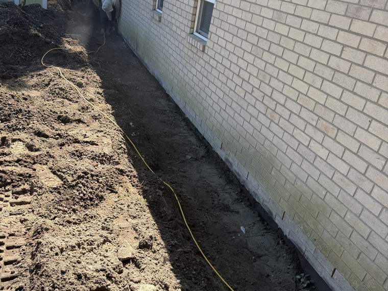 Drainage trench opened tight along a brick foundation wall