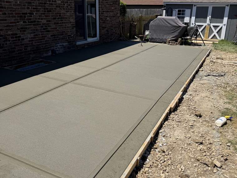 Large concrete patio slab poured along the back of a brick house