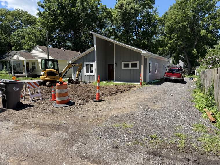 Compact excavator and traffic cones set up for site work in front of a home