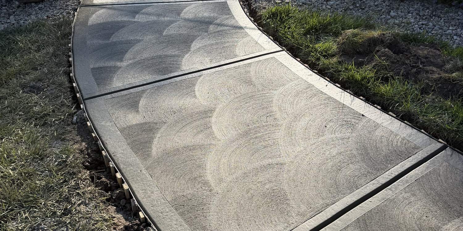 Swirl finished concrete walkway curving through a landscaped bed