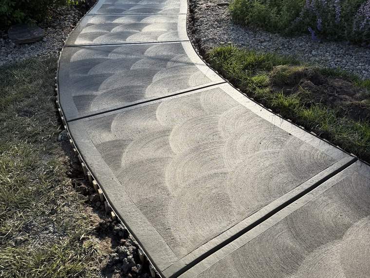 Swirl finished concrete walkway curving through a landscaped bed