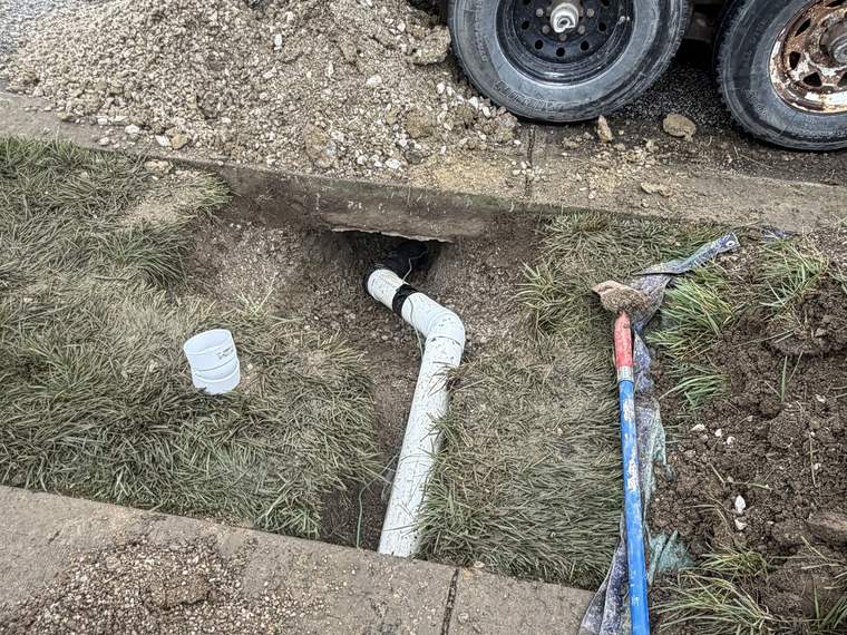 Utility trench opened at a sidewalk with a dump trailer staged for spoil